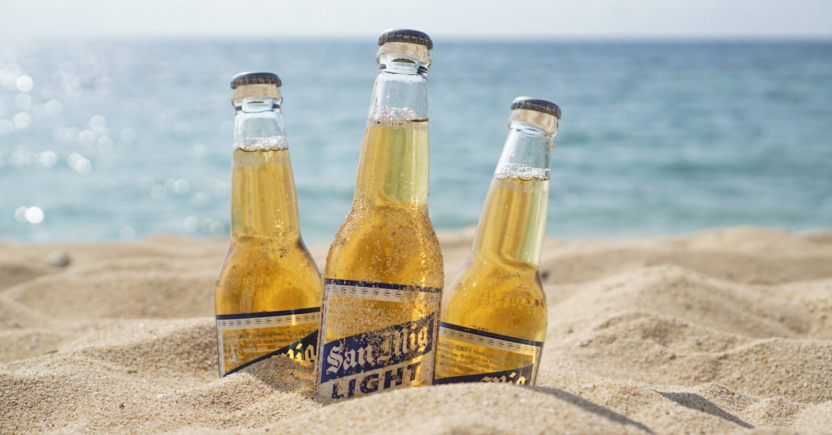 Three beer bottles in sand by the beach.