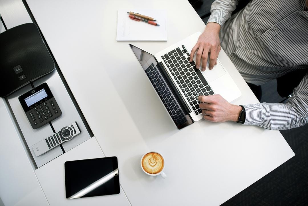 Person working on laptop at desk with coffee.