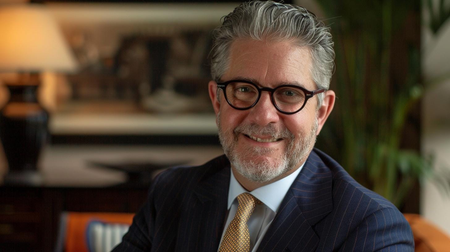 Smiling man in suit with glasses and gray hair.