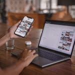 hand typing on a laptop and holding a phone