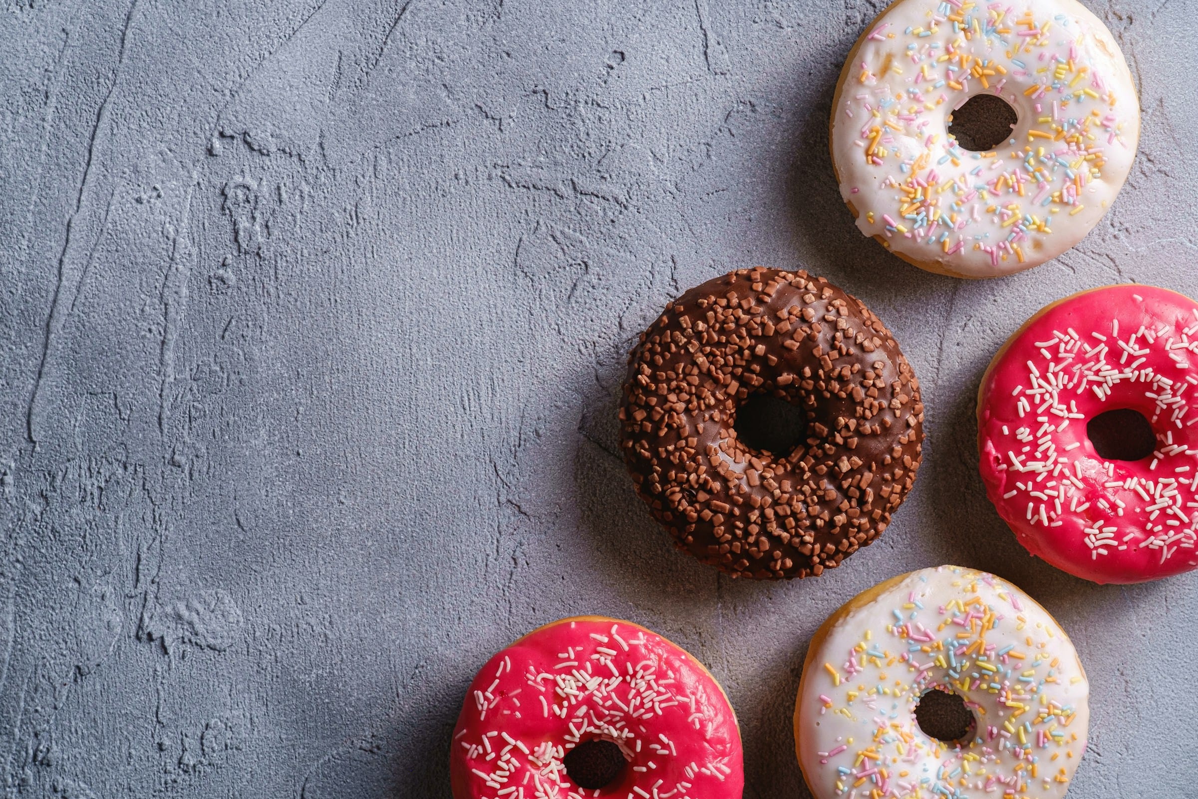 Assorted donuts with sprinkles on gray background.