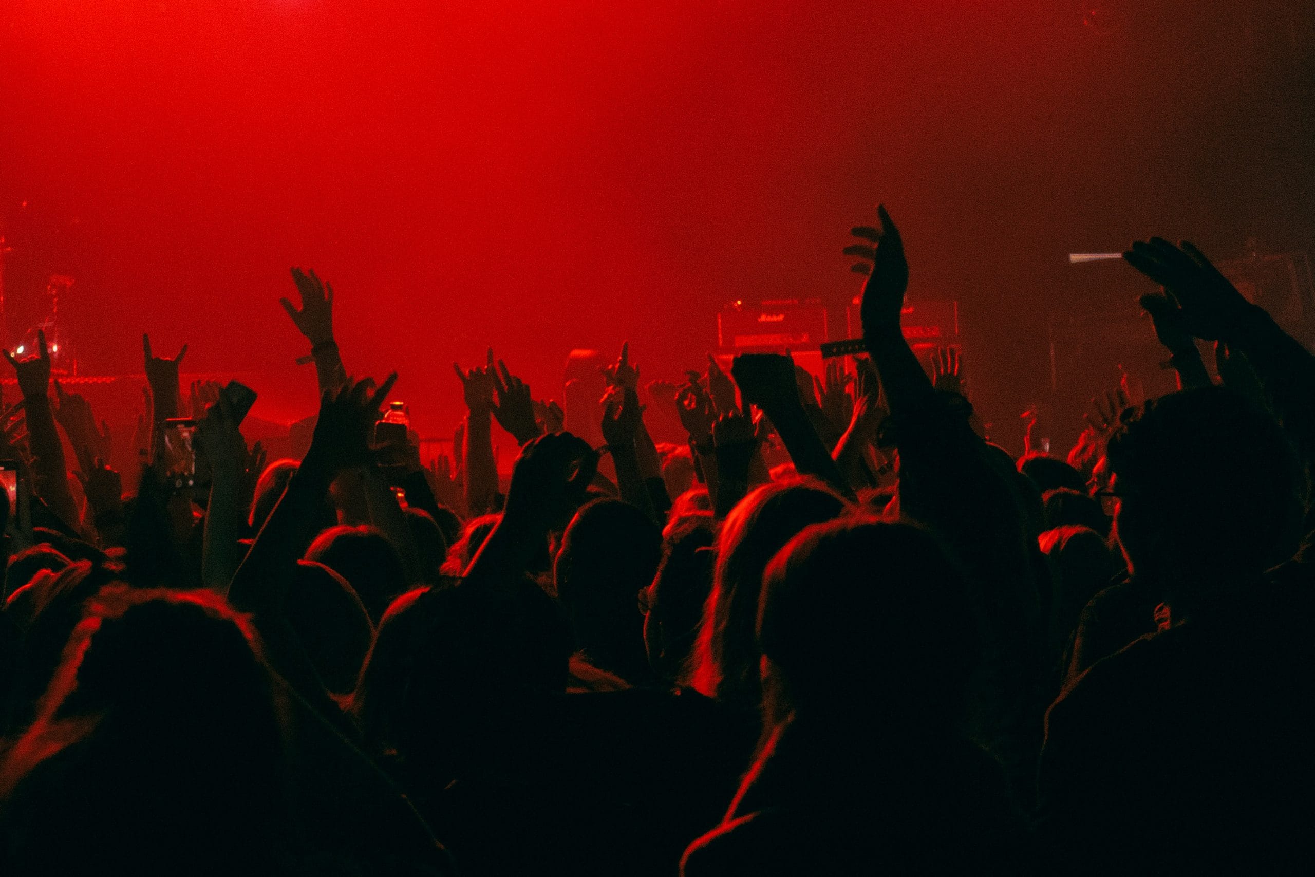 Crowd at concert with red lighting, hands raised.