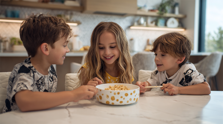 Three kids enjoying cereal around a kitchen table.