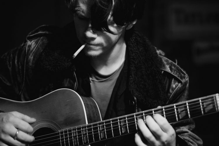 Man playing acoustic guitar in dark setting.