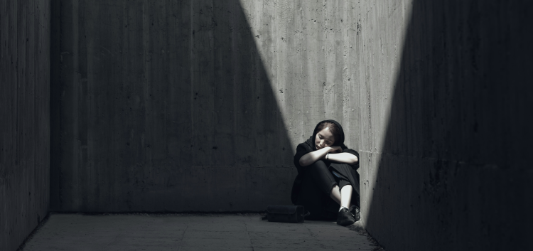 Person sitting alone in dark concrete corner.