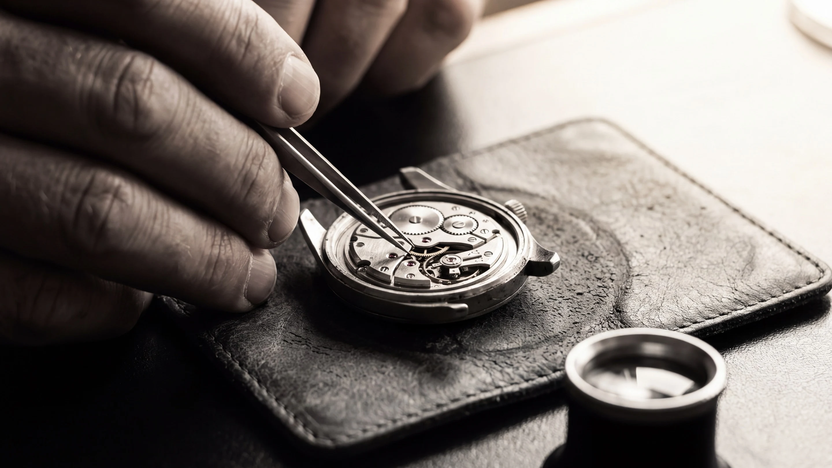 A watchmaker’s hand holding fine tweezers over an open mechanical watch movement, every gear in view